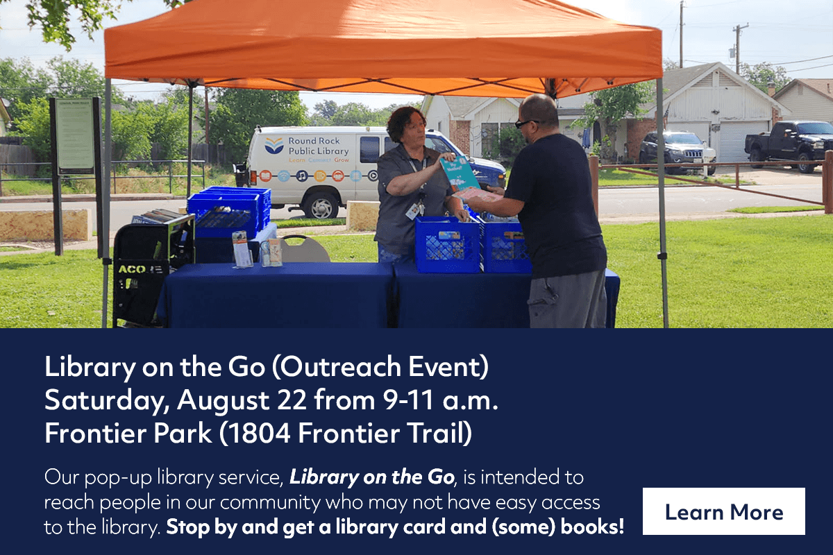 A library staff member stands under an orange tent at Frontier Park, handing a library card to a visitor during an outdoor Library on the Go event. Tables with supplies and a library van are visible in the background.