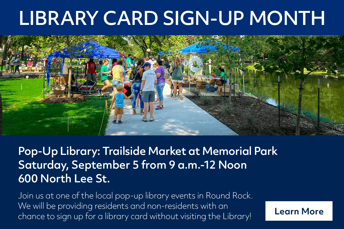 People gather at a pop-up library tent in a park, surrounded by trees and a pond, during a community event for Library Card Sign-Up Month.