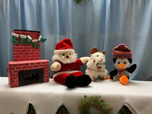 Puppets depicting Santa, a mouse and a penguin sit among Christmas decorations