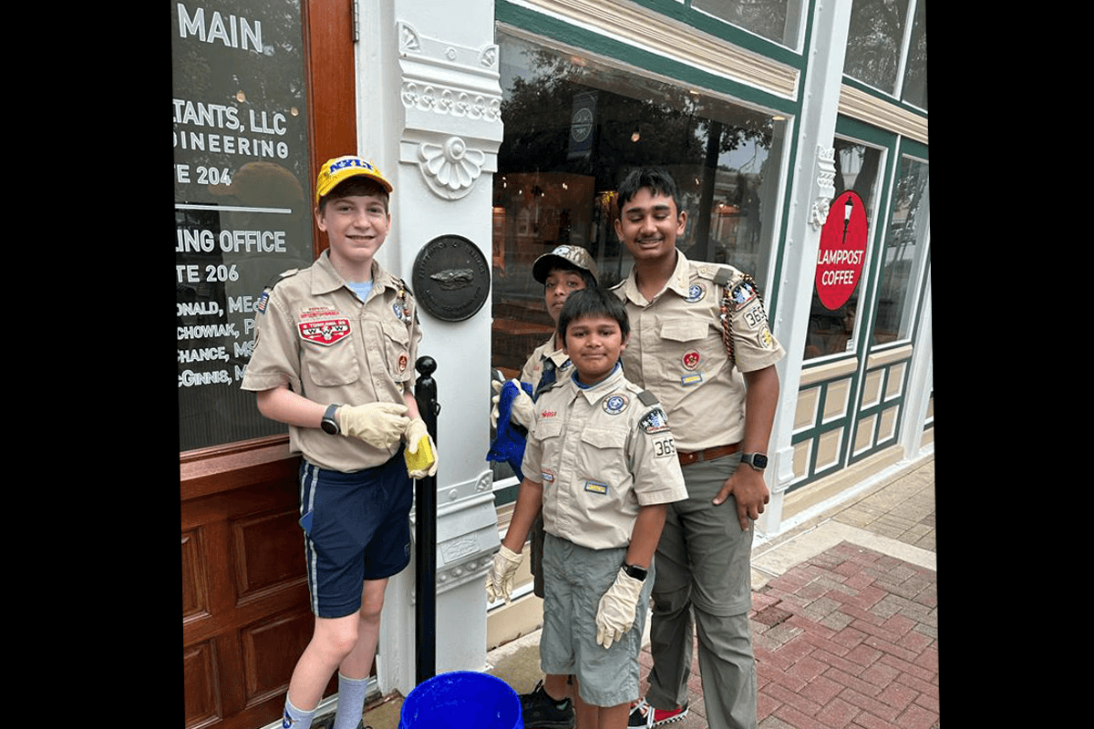 Four Boy Scouts cleaning a historic marker on the wall of a building