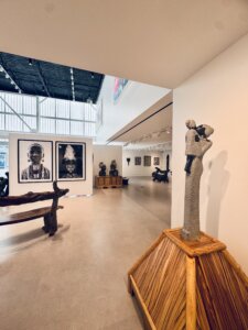 A modern art gallery near me with sculptures and framed black-and-white portraits; a stone sculpture on a wooden stand is in the foreground, with benches and more artworks in the background. Perfect for music and arts Round Rock enthusiasts.