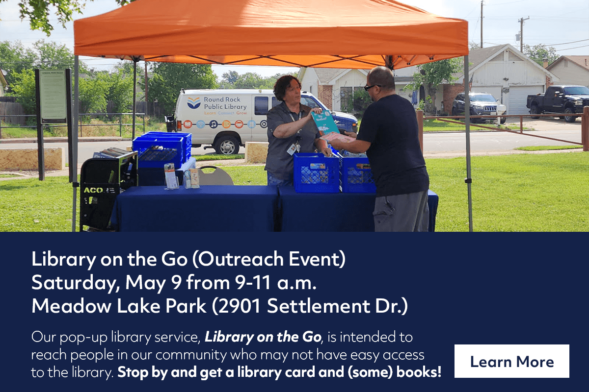 A library staff member sets up a pop-up library booth under an orange canopy in a park, with a sign promoting the Library on the Go outreach event at Meadow Lake Park on Saturday, May 9.