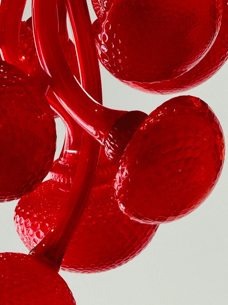 Close-up of several textured, bright red, glass-like objects with a glossy surface, curving stems, and a honeycomb pattern, clustered together against a light gray background—an eye-catching piece reminiscent of works often featured in an art gallery near me.