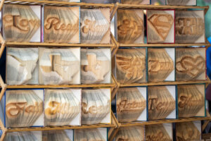 Books with folded and carved pages form 3D shapes and words, including Read, symbols, and logos, displayed on a wooden shelf. Designs are intricate and vary across each book.
