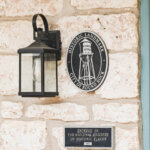 A stone wall displays a lantern, a round Historic Landmark City of Round Rock plaque, and a rectangular plaque noting entry in the National Register of Historic Places in 1983.