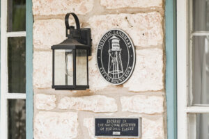 A stone wall displays a lantern, a round Historic Landmark City of Round Rock plaque, and a rectangular plaque noting entry in the National Register of Historic Places in 1983.