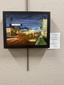 A painting of a city street at night with bright lights, a DOWNTOWN sign, and blurred streets. The artwork is displayed on a beige wall with a price tag of $320.